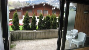 Blick von einem Balkon mit Betonboden, Holzlattenzaun und einem Gebäude mit mehreren Fenstern im Hintergrund.
