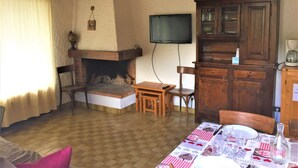 A cozy living room with a fireplace, wooden furniture, a television mounted on the wall, and a dining area with a table set for two. - 1-bedroom near slopes with balcony (La Clusaz)