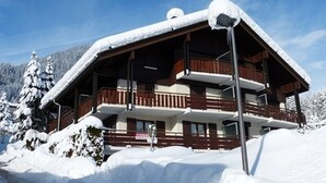 A multi-story wooden lodge with balconies, surrounded by snow-covered trees and a clear sky. - 1-bedroom near slopes with balcony (La Clusaz)