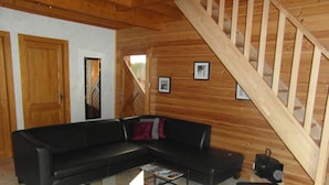 Una sala de estar con un sofá de cuero negro, una mesa de centro de vidrio y una escalera de madera.
