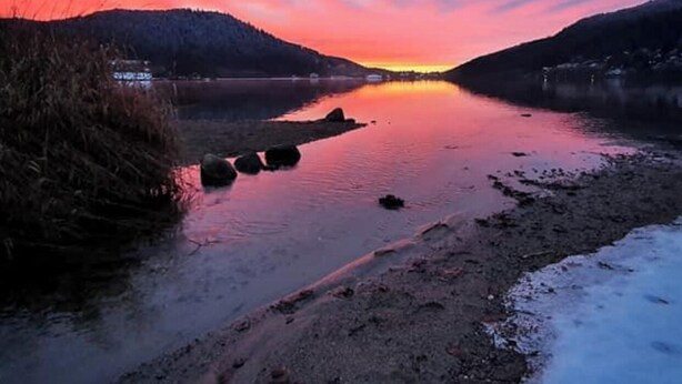 Un río con un atardecer, agua tranquila y una orilla nevada.