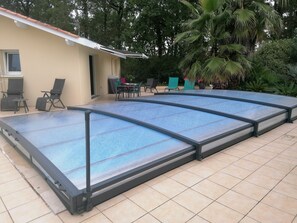 A covered outdoor swimming pool with a tiled floor and a covered patio area with chairs and a table.