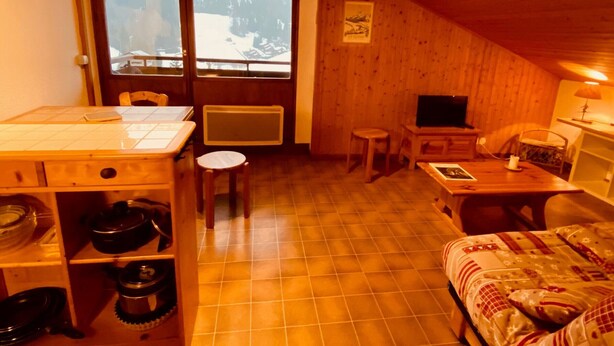 A cozy wooden cabin with a dining area, a TV, and a bed. - Cozy 2-Room Apartment with Balcony and Mountain View in La Clusaz (La Clusaz)