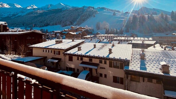 Une ville de montagne enneigée, avec des bâtiments et une piste de ski en arrière-plan.