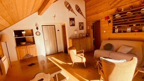 Un intérieur chaleureux, avec des éléments en bois, comprenant un coin repas, un canapé et des étagères ornées d’objets décoratifs.