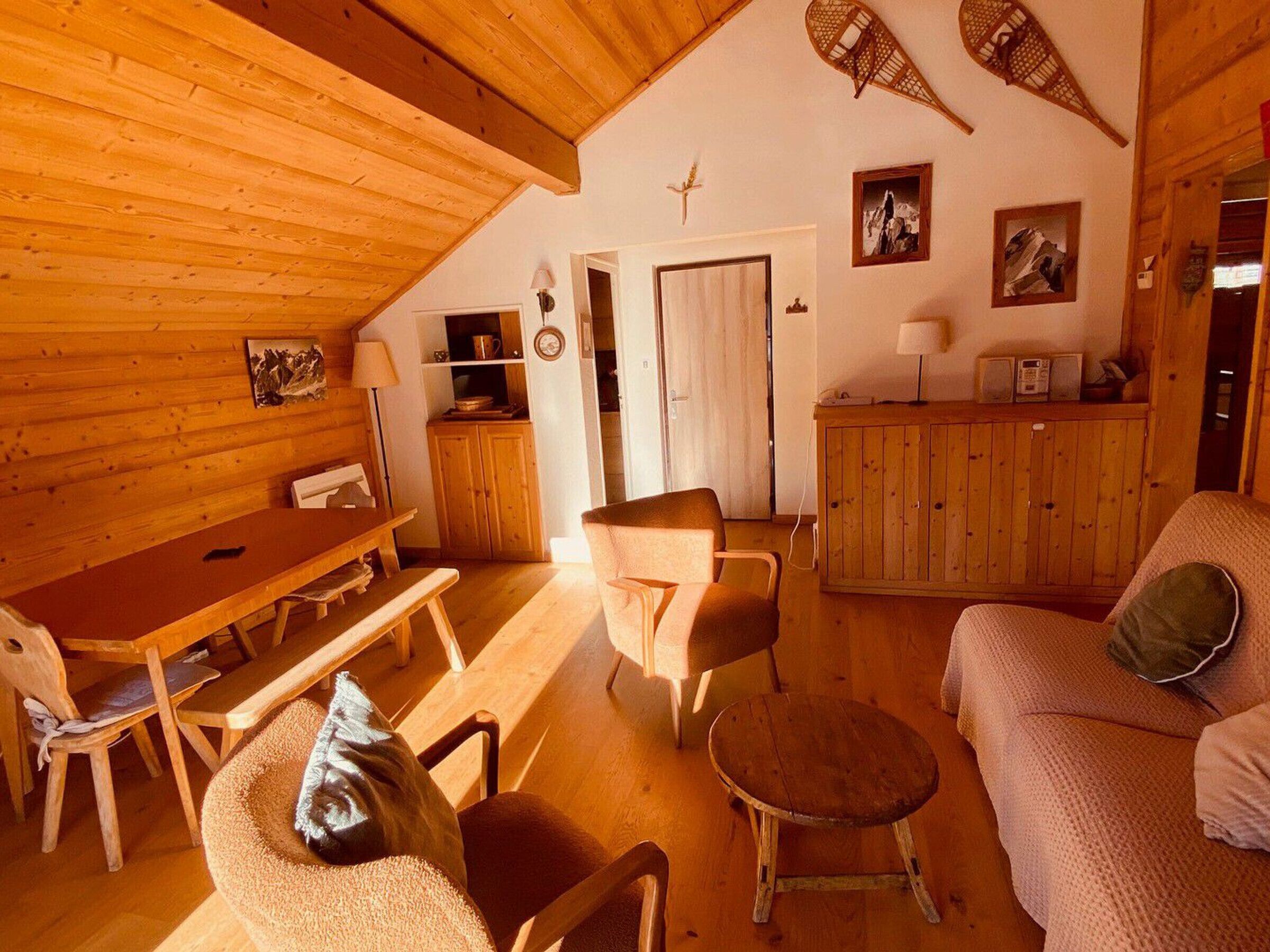 A cozy cabin interior with a wooden dining table, chairs, a sofa, and a small round table.