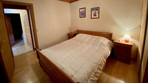 A bedroom with a wooden bed frame, a nightstand with a lamp, and two framed pictures on the wall. - 3-room apartment with balcony, fireplace, and Wifi in La Clusaz (La Clusaz)