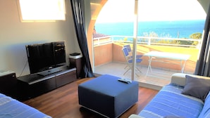 A hotel room with a balcony, a TV, a sofa, and a bed. - Beautiful duplex design air-conditioned single storey facing the sea (Monticello)