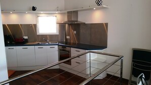 A modern kitchen with white cabinets, stainless steel appliances, and a black countertop. - Beautiful duplex design air-conditioned single storey facing the sea (Monticello)