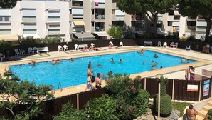 A swimming pool surrounded by lounge chairs and a multi-story building with balconies. - for rent studio gruissan (gruissan)