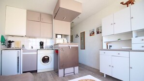 A compact kitchen with a washing machine, a refrigerator, and a dining area with a woven basket. - for rent studio gruissan (gruissan)