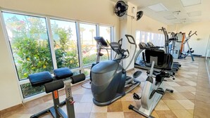 A gym with cardio machines, weight benches, and a large window with a view of greenery. - 𝔾𝕦𝕝𝕗𝔽𝕣𝕠𝕟𝕥 𝑬𝒎𝒆𝒓𝒂𝒍𝒅 𝑰𝒔𝒍𝒆 9th Floor Stocked & Stellar Reviews! (Unknown)