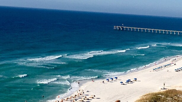 A beach with a pier extending into the ocean, sandy beach, and umbrellas. - 𝔾𝕦𝕝𝕗𝔽𝕣𝕠𝕟𝕥 𝑬𝒎𝒆𝒓𝒂𝒍𝒅 𝑰𝒔𝒍𝒆 9th Floor Stocked & Stellar Reviews! (Unknown)