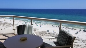 A balcony with a view of a beach and ocean. There are striped chairs and a round table with a decorative item on it. - 𝔾𝕦𝕝𝕗𝔽𝕣𝕠𝕟𝕥 𝑬𝒎𝒆𝒓𝒂𝒍𝒅 𝑰𝒔𝒍𝒆 9th Floor Stocked & Stellar Reviews! (Unknown)