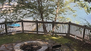 A stone fire pit with a bench, surrounded by a wooden fence, overlooking a body of water.