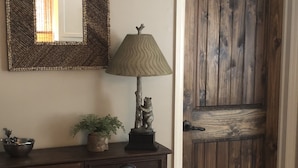A wooden door with a rustic finish, a dark wooden cabinet with drawers, a wall-mounted mirror, and a lamp with a textured lampshade.