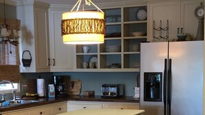 A modern kitchen with a central island, bar stools, a refrigerator, and a chandelier.