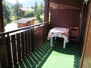 A balcony with a table covered in a tablecloth, a chair, and a view of houses and trees in the background.