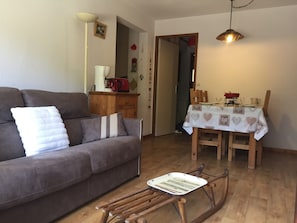 A living room with a sofa, a dining table set with a tablecloth, and a wooden rocking chair. - Cozy 3-room, ski-in/ski-out, parking, WiFi, La Clusaz (La Clusaz)