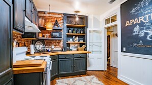 A kitchen with dark cabinets, a wooden countertop, a brick wall, and a vintage clock.