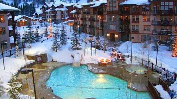 Een resort met meerdere gebouwen, een centraal gelegen zwembad en besneeuwde omgeving.