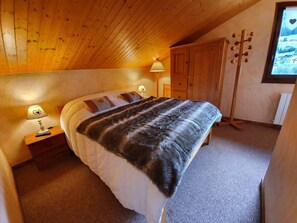 Een slaapkamer met een bed, een nachtkastje met een lamp, een houten garderobe en een houten vloer.