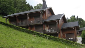 Una casa de madera de varios pisos con balcones en cada nivel, ubicada en una ladera cubierta de hierba.