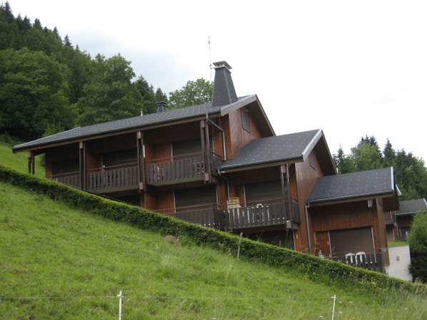 Une maison en bois à plusieurs étages, dotée de balcons à chaque niveau, située sur une colline verdoyante.