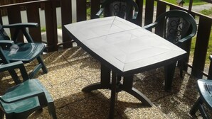 Una terraza con mesa y sillas, baranda de madera y vista a edificios al fondo.