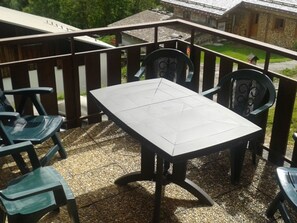 Een terras met een tafel en stoelen, een houten hekwerk en gebouwen in de verte.