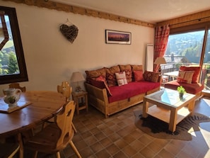 Un salon chaleureux avec un canapé en bois, une table à manger et une vue sur l’extérieur.