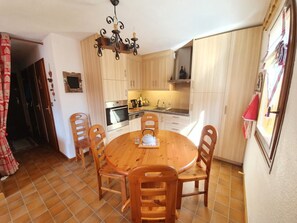 Een kleine keuken met een ronde houten tafel, vier stoelen en eenvoudige apparaten.