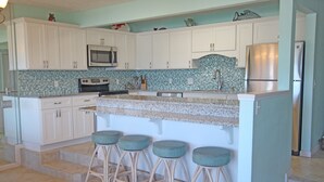 A kitchen with white cabinets, a tiled backsplash, a stainless steel refrigerator, and three bar stools. - Exquisite 1st-Floor Panama City Beachfront, Low Density, Step from Deck to Sand  (Panama City Beach)