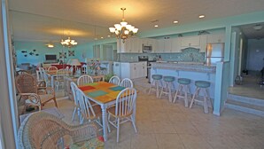 A spacious kitchen with white cabinets, a central island with stools, and a dining area with a colorful table and wicker chairs. - Exquisite 1st-Floor Panama City Beachfront, Low Density, Step from Deck to Sand  (Panama City Beach)