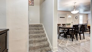Una escalera conduce a un comedor con una araña, un reloj y una puerta.