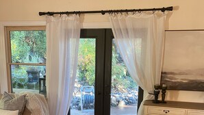 A cozy living room with a leather sofa, a white cabinet, and a large window with sheer curtains.