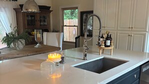 A kitchen with a large island, white countertops, dark cabinetry, and pendant lighting.