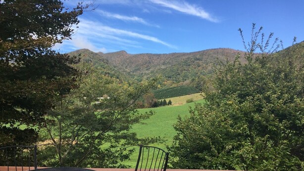 Eine Terrasse mit Tisch und Stühlen mit Blick auf ein grünes Tal und Hügel.