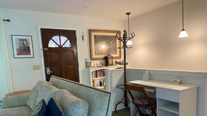 Ein gemütliches Wohnzimmer mit einem grauen Sofa, einem Holzsessel, einem weißen Schreibtisch und einem Bücherregal.