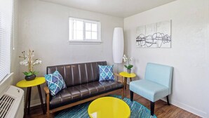 A living room with a brown leather sofa, a blue armchair, a yellow round table, and a small yellow table with a plant. - Affordable for Long Stay, Great for Budget-Friendly Business Travels (Oklahoma City)