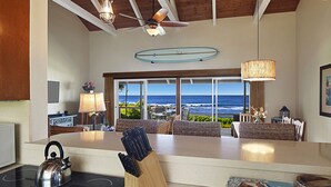 Una cocina con una isla grande, una tetera y un bloque de cuchillos. Se ve el océano a través de ventanas amplias.