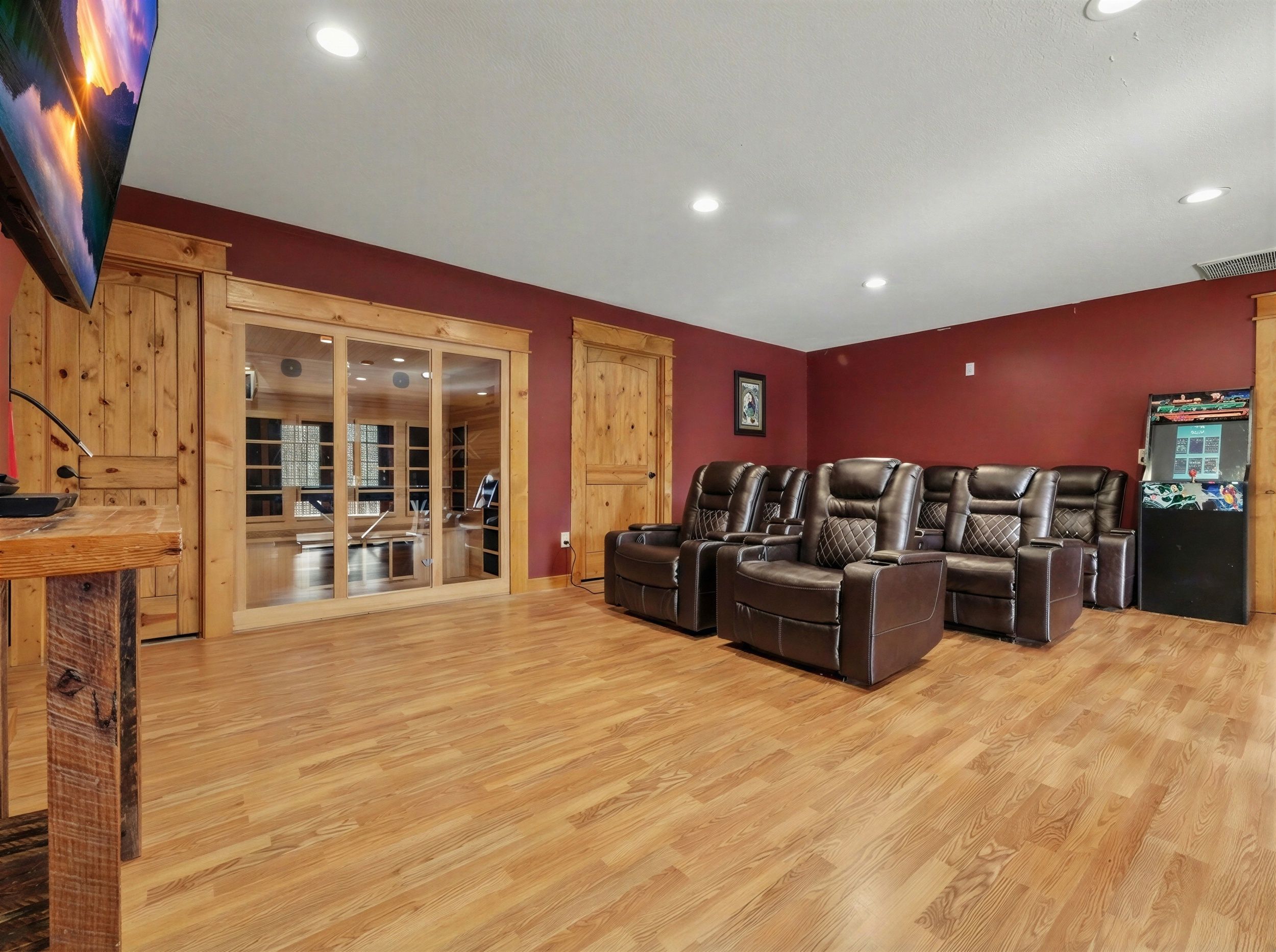 A room with wooden flooring, a television, and a seating area with leather recliners.