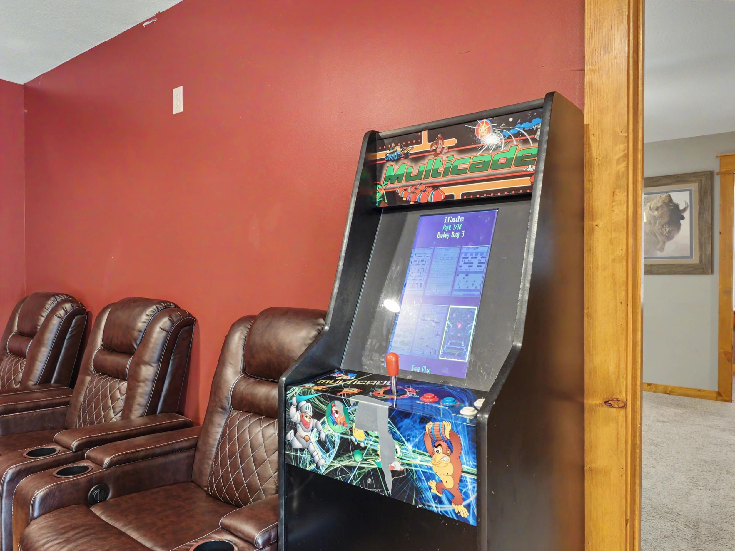 Una sala de juegos con videojuegos Multicade e iCade, sillones de cuero reclinables y un cuadro en la pared.