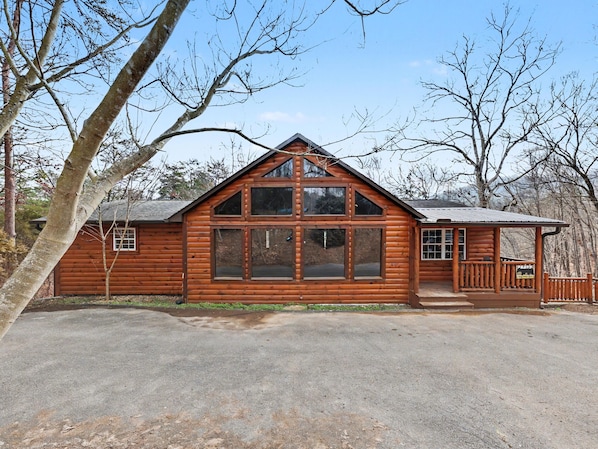 A log cabin with a large front window, a porch, and a garage.