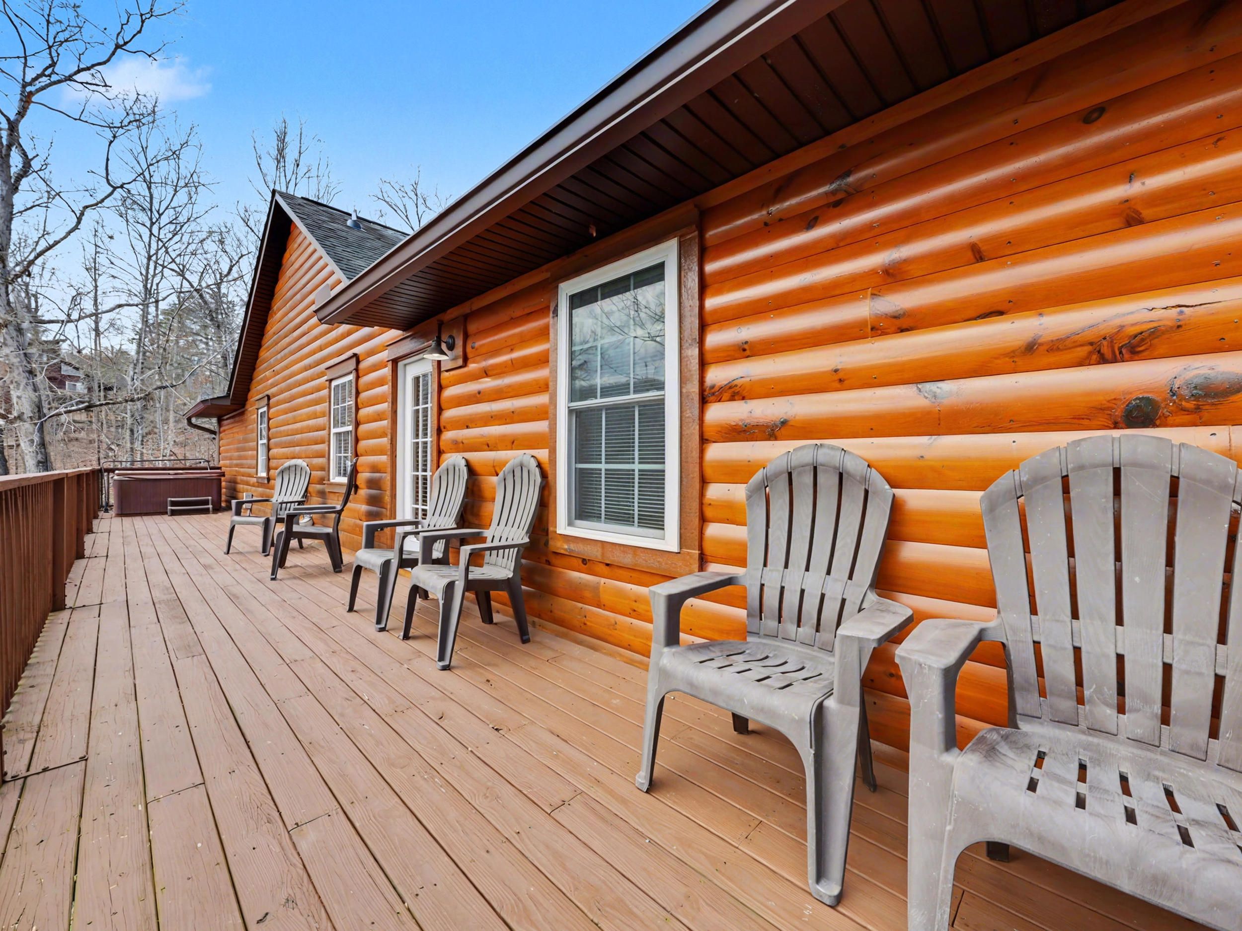 Una cabaña de troncos con terraza de madera, mobiliario exterior y un jacuzzi.
