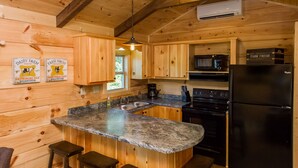 Cocina de cabaña de madera con encimera de granito, pileta de acero inoxidable, electrodomésticos negros y taburetes de bar de madera.