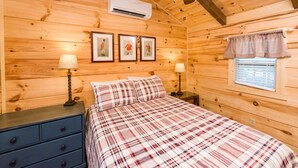 Un dormitorio de cabaña de madera con una cama, dos mesitas de noche con lámparas, un ventilador de techo y cuadros enmarcados en la pared.