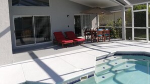 A covered outdoor area with a pool, red lounge chairs, and a table with chairs. - Villa Bonita. Southern Dunes 4 star golf course. Disney and Legoland area. (Haines City)
