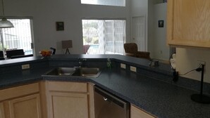 A kitchen with a large island, a dishwasher, and a sink. There are two windows with blinds, a ceiling light, and a door. - Villa Bonita. Southern Dunes 4 star golf course. Disney and Legoland area. (Haines City)