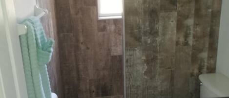 Un baño con pared de madera, inodoro blanco y zona de ducha.
